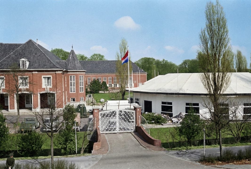 An old color photo of the Princess Juliana Barracks in The Hague. It shows large red brick buildings, a white gate, and a Dutch flag flying in the wind on a sunny day in 1964 An old color photo of the Princess Juliana Barracks in The Hague. It shows large red brick buildings, a white gate, and a Dutch flag flying in the wind on a sunny day in 1964