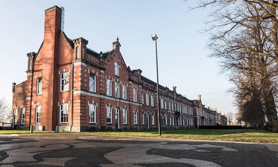 A wide-angle view of the long, red-brick Neo-Renaissance facade of the Johan Willem Friso Barracks in Assen, featuring decorative masonry and historical architectural details. A wide-angle view of the long, red-brick Neo-Renaissance facade of the Johan Willem Friso Barracks in Assen, featuring decorative masonry and historical architectural details.